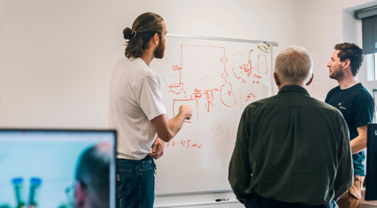 Three engineers talking in front of a white board covered in graphs and writing.